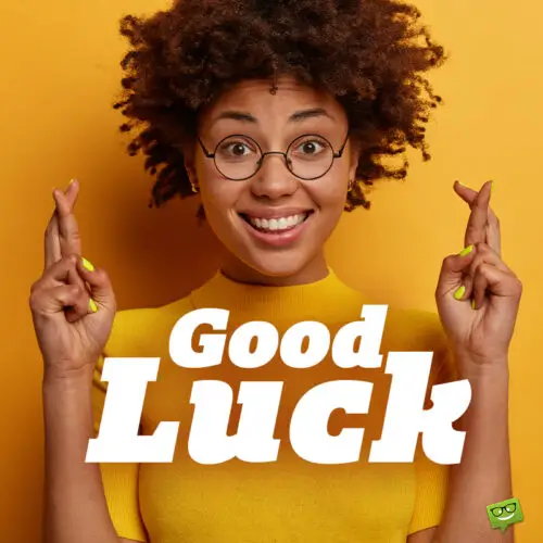 Good luck image with beautiful girl crossing fingers in front of yellow background.