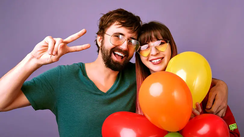 Featured image for a blog post with Instagram Captions about birthday balloons. On the image there is a beautiful woman and a handsome man holding balloons and celebrating.