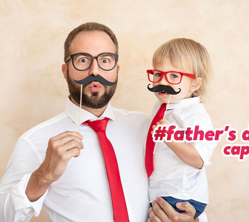 Featured image for an article with father's day captions. On the image we see a handsome father with his child, both putting on funny mustaches on their faces.